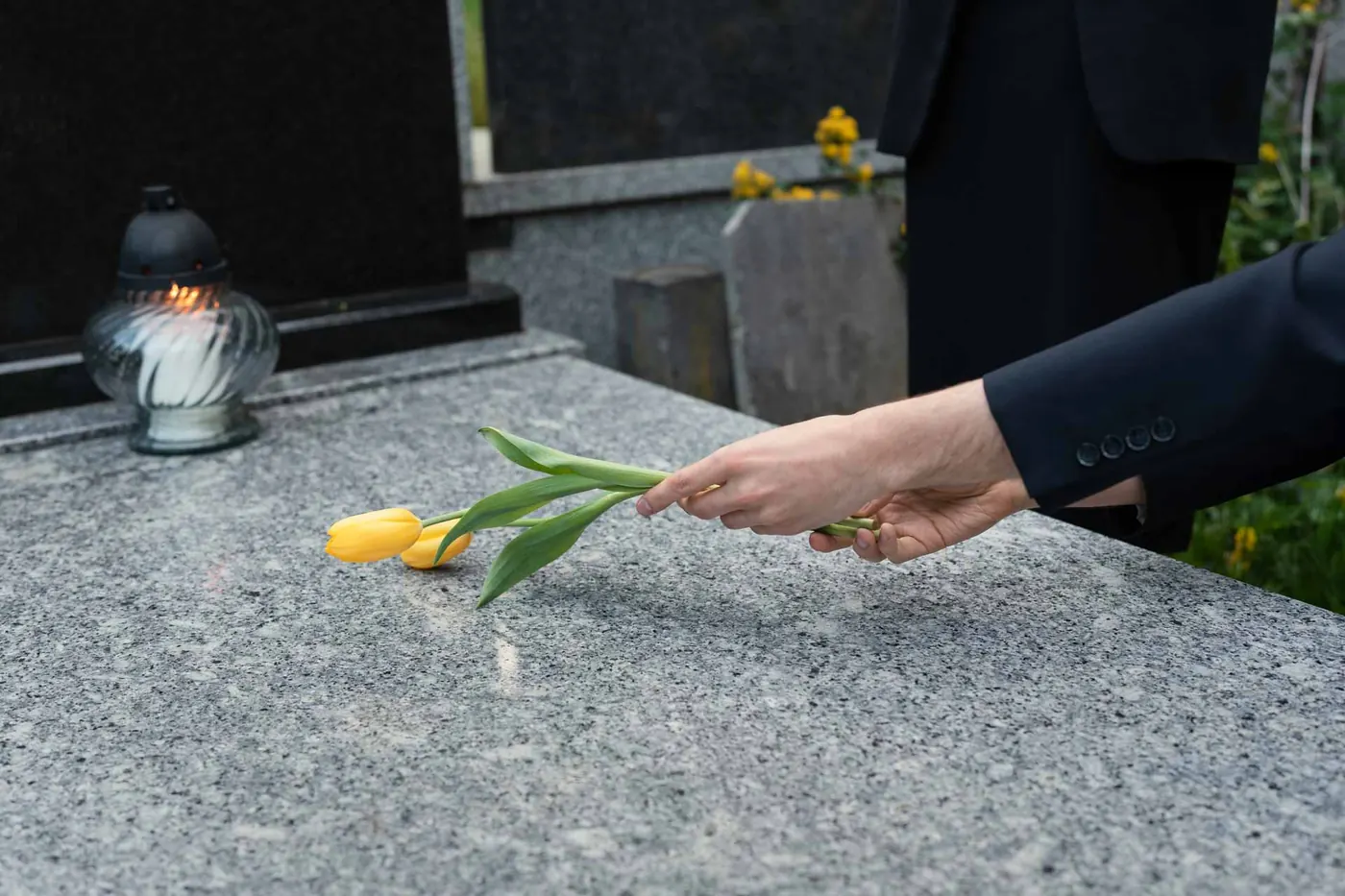 Hand legt gelbe Tulpen auf einen Grabstein