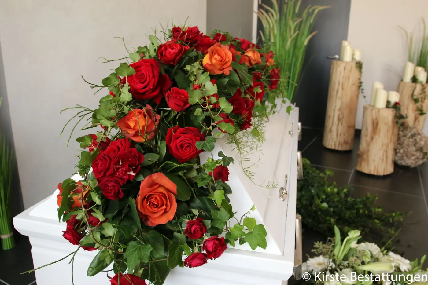 Rote und orange Rosen auf weißem Sarg