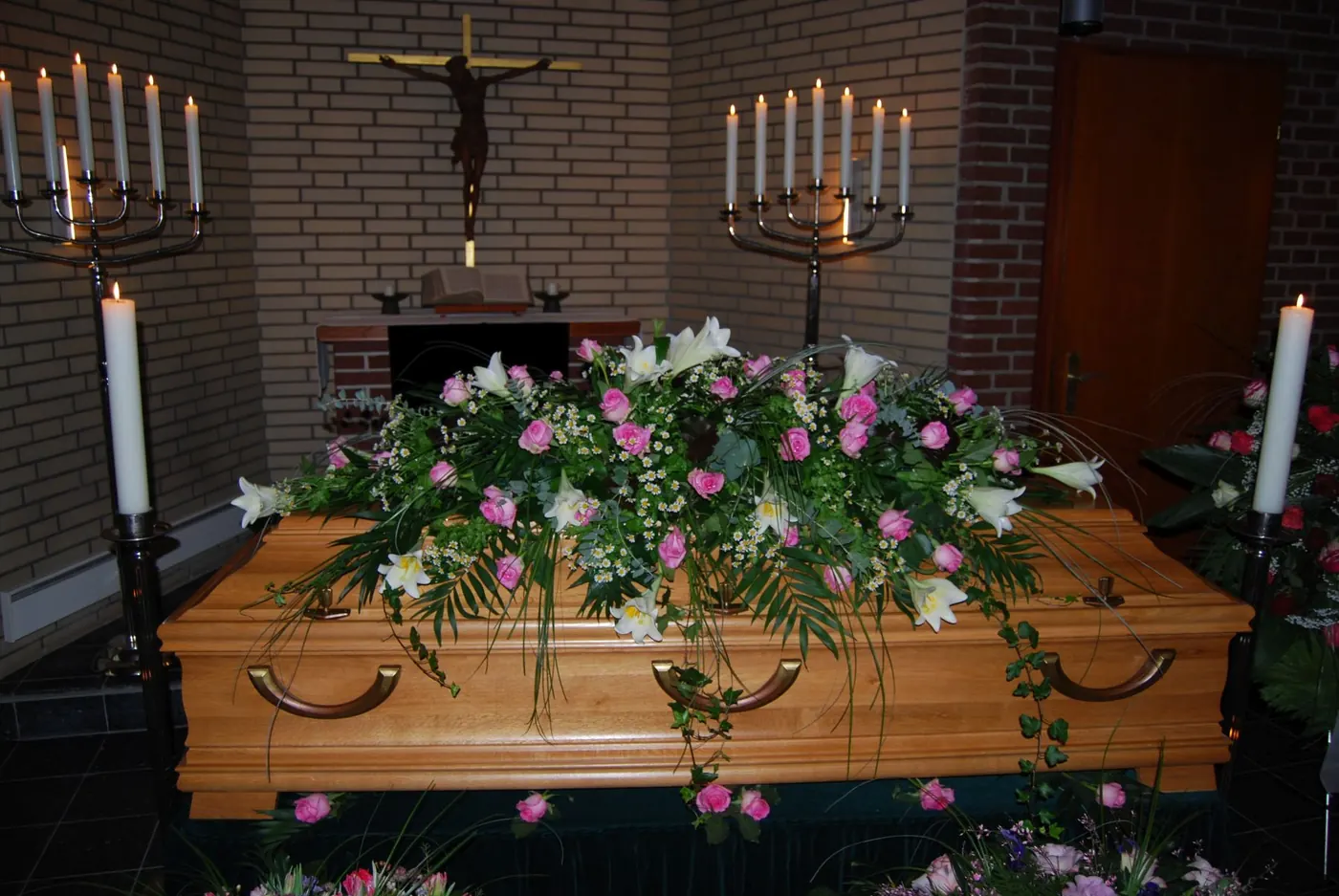 Holzsarg mit Blumen unter Kerzenleuchtern