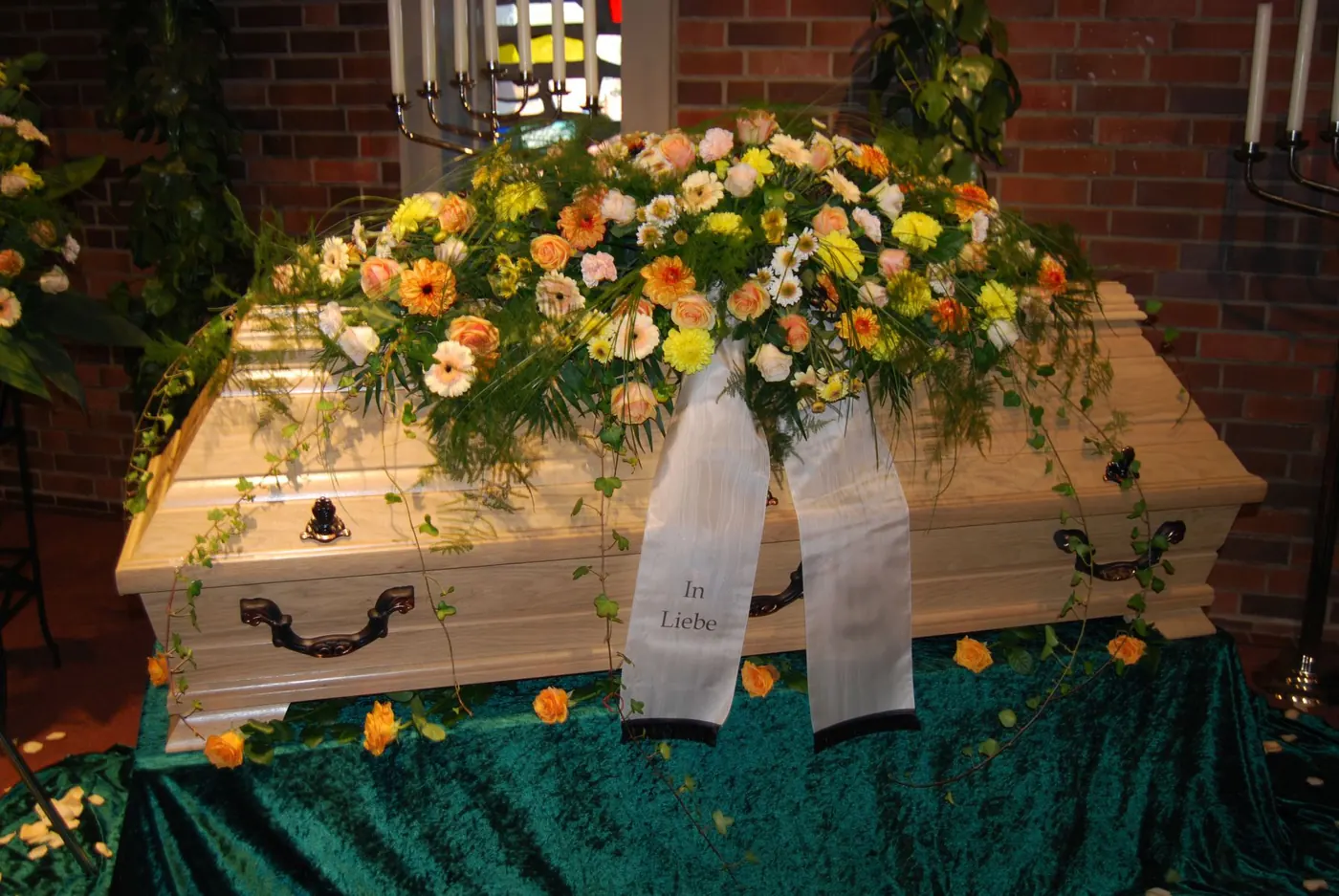 Heller Holzsarg mit gelb-orangem Blumengesteck
