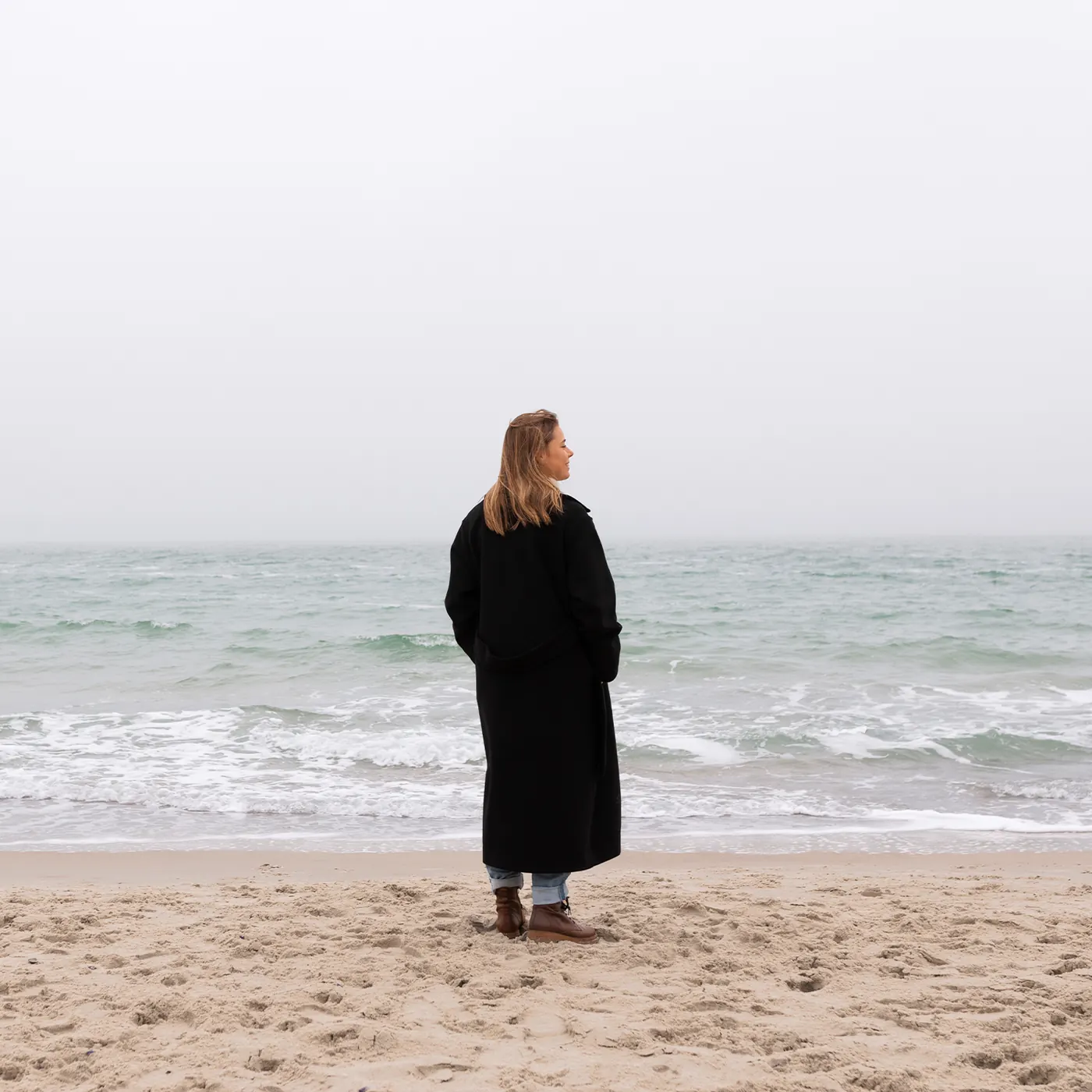 Frau im dunklen Mantel am Meer
