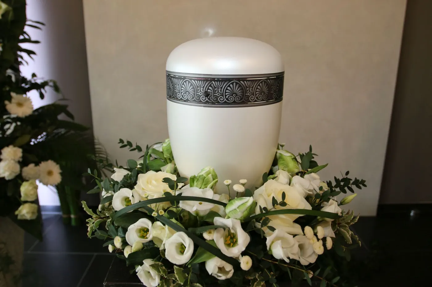 Weiße Urne mit Zierband inmitten weißer Blüten