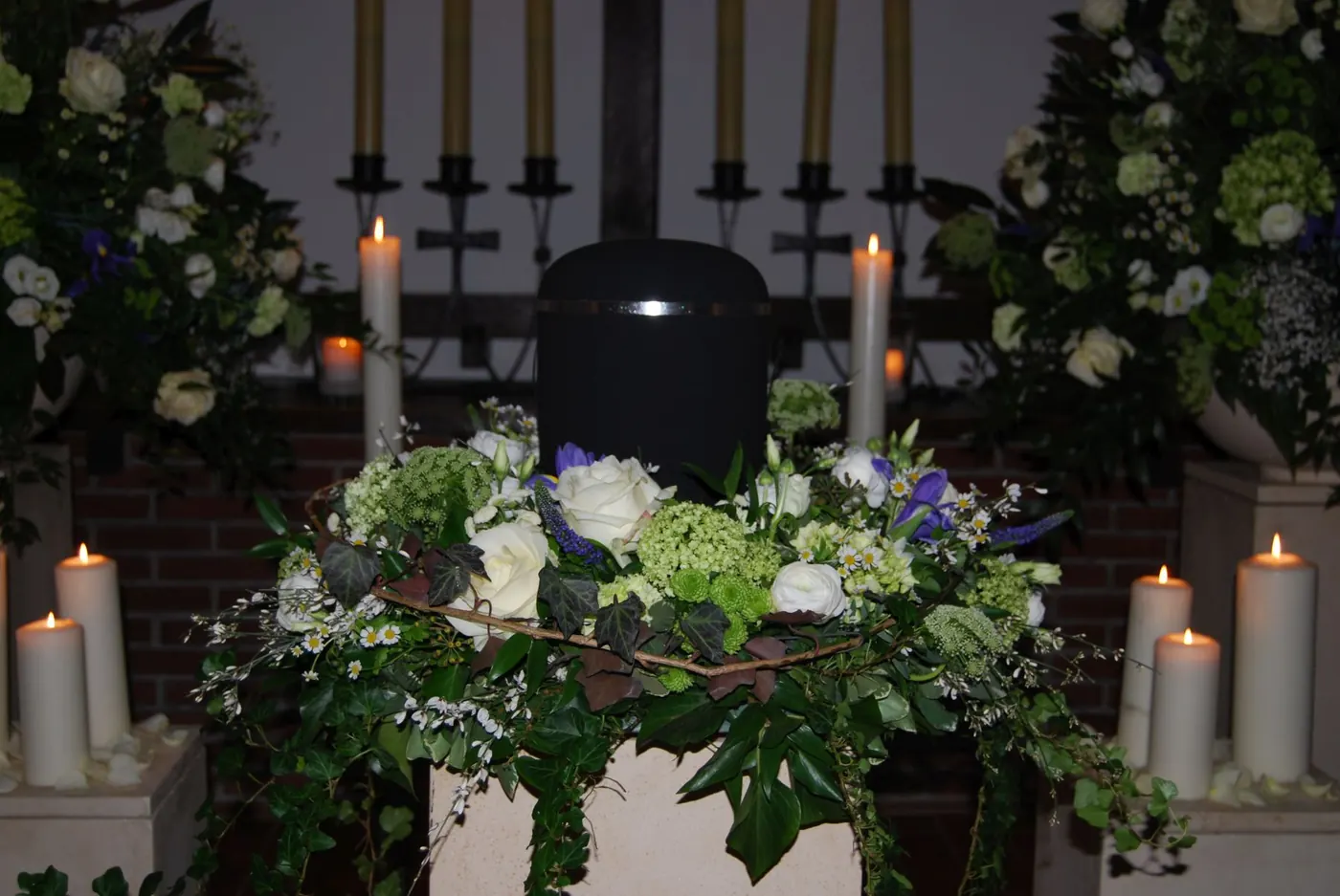 Dunkle Urne mit grüner und weißer Floristik vor Kerzen