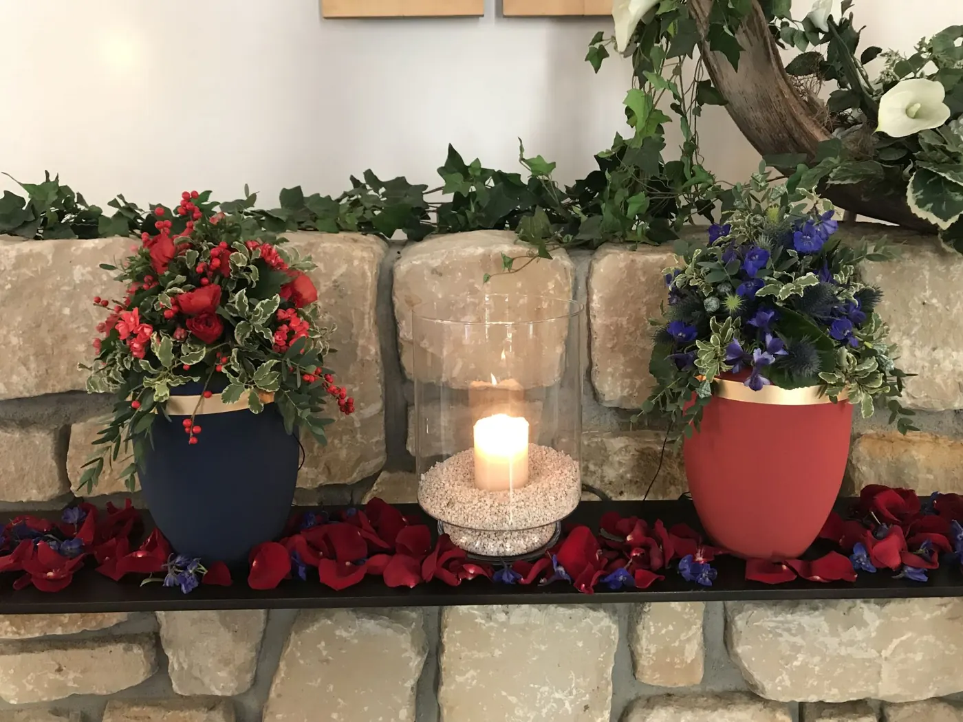 Zwei Urnen auf Steinmauer mit Rosen und Kerze