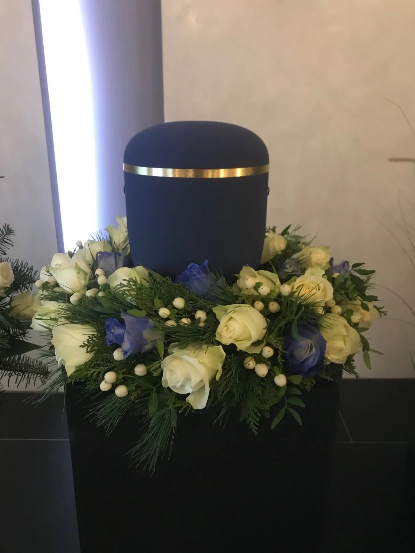 Dunkelblaue Urne in weiß-blauem Blumenkranz
